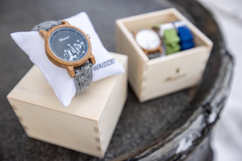 Wooden wristwatch with grey felt strap on pillow in front of box with extra straps and second watch | © Planai-Hochwurzen-Bahnen Gesellschaft m.b.H.