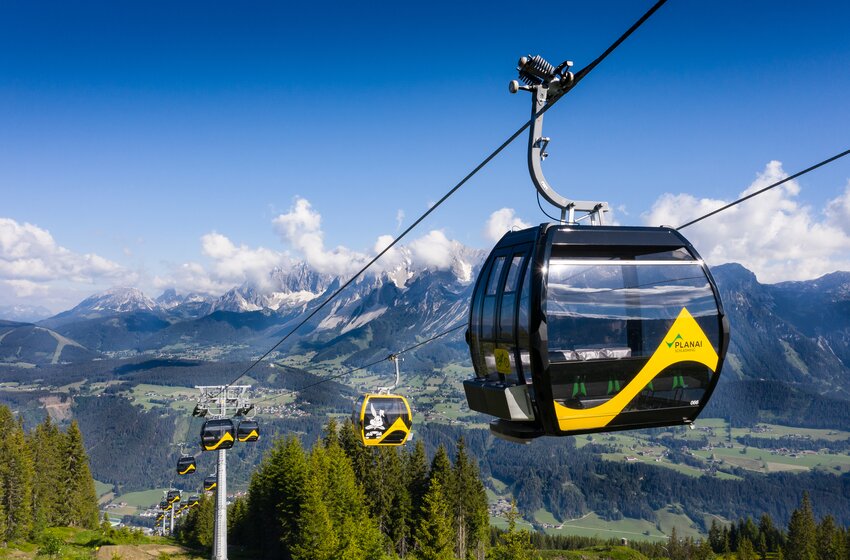Modern Planai gondolas float above green slopes with a scenic view of the Dachstein mountains and sunlit alpine valleys | © Planai-Hochwurzen-Bahnen GmbH