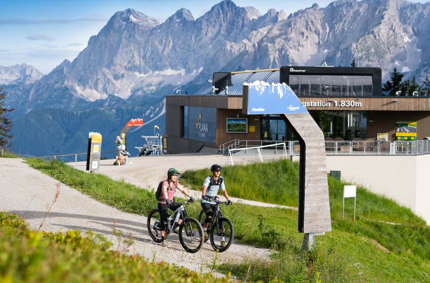 Start of the Flowline at Bikepark Planai next to top station at 1830 m | © Planai-Hochwurzen-Bahnen GesmbH Two mountain bikers at Flowline start near Planai top station at 1830 m, with Dachstein range rising in the background | © Planai-Hochwurzen-Bahnen GesmbH