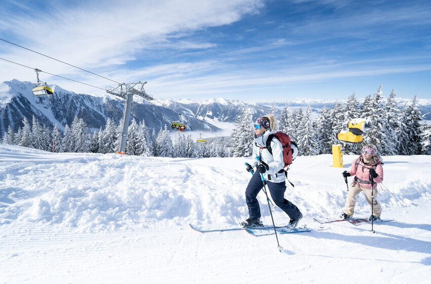 Two ski tourers hiking through snowy slopes on the Planai Two ski tourers hike up snowy Planai slope in sunshine with panoramic mountain views in the background.