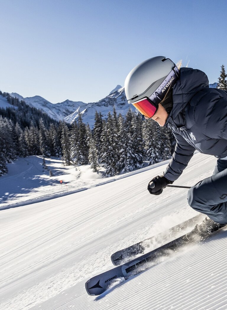 Dynamische Skifahrerin bei perfektem Carving auf Traum-Piste | © Planai-Hochwurzen-Bahnen Gesellschaft m.b.H. Skifahrerin carvt schwungvoll auf frisch präparierter Piste bei Sonne vor verschneiten Bäumen und Bergen. | © Planai-Hochwurzen-Bahnen Gesellschaft m.b.H.