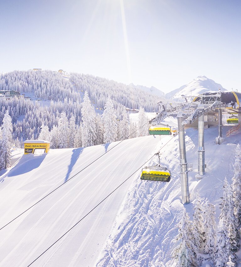 Yellow chairlift passes snowy trees on sunny Lärchenkogel on the Planai | © Planai-Hochwurzen-Bahnen Gesellschaft m.b.H.