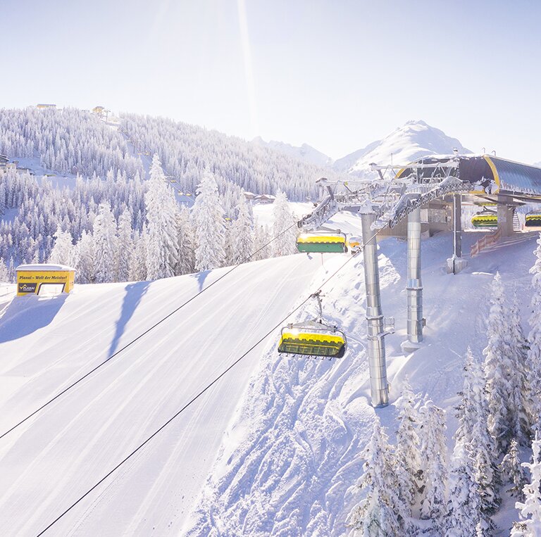 Yellow chairlift passes snowy trees on sunny Lärchenkogel on the Planai | © Planai-Hochwurzen-Bahnen GmbH