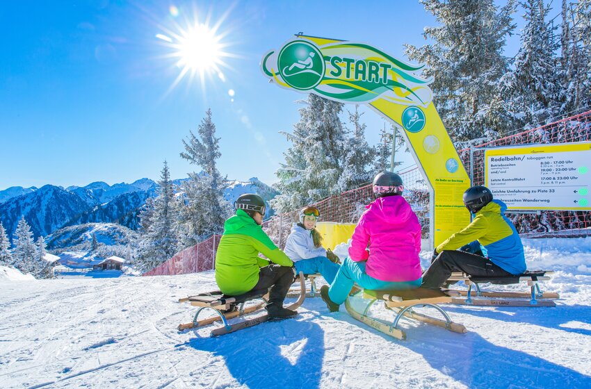 Rodelspaß bei Sonnenschein am Start der Rodelbahn Hochwurzen | © Planai-Hochwurzen-Bahnen Gesellschaft m.b.H. Vier Rodler:innen sitzen an sonniger Rodelbahn-Startlinie mit Blick auf verschneite Berge. | © Planai-Hochwurzen-Bahnen Gesellschaft m.b.H.