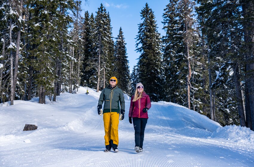 Ein Paar spaziert auf präpariertem Winterweg durch verschneiten Wald bei Sonnenschein und klarer Winterluft. | © Winterwanderbilder (c) Gerald Oberreiter
