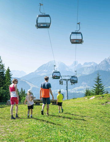 Family hikes on sunny alpine meadow, gondolas pass by in front of a stunning mountain panorama | © Ski amadé GmbH